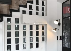 Mur blanc moderne avec des décorations rectangulaires noires, un climatiseur mural et deux lampes murales réglables sous un escalier.
