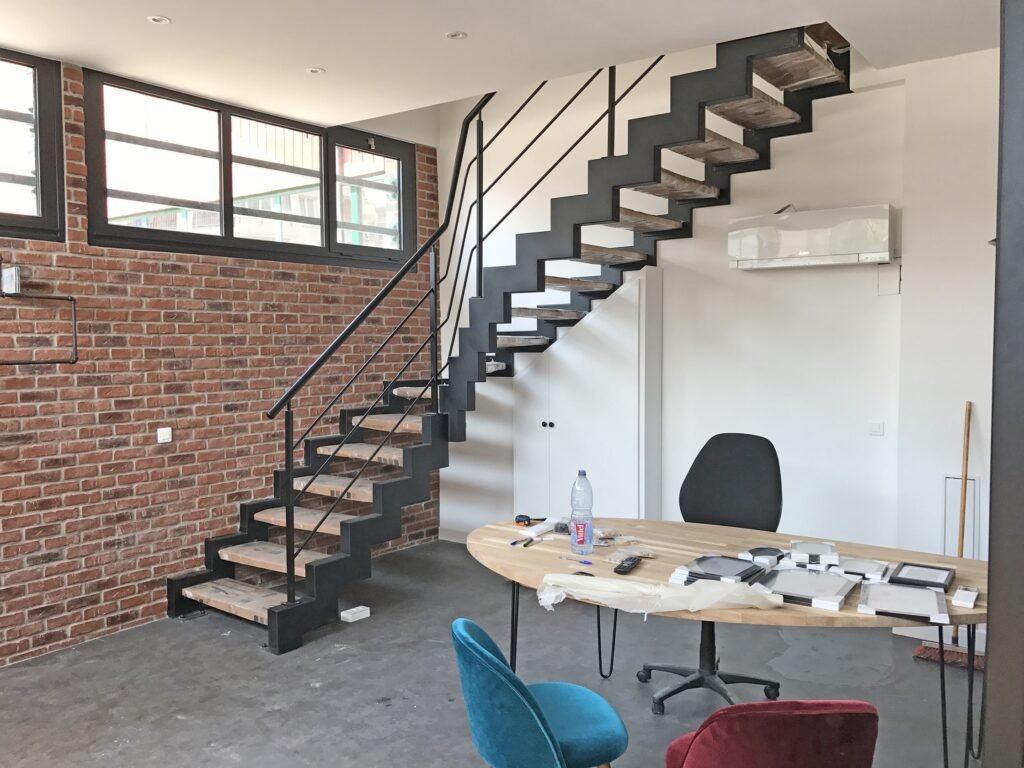 Un bureau moderne avec un mur d'accent en briques, un escalier en métal et un bureau avec des fournitures de bureau.