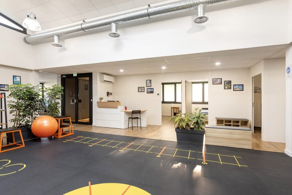Intérieur d'un bureau ou d'une clinique moderne avec un bureau d'accueil, des plantes d'intérieur, des œuvres d'art murales, des sièges et des appareils d'exercice sur un sol noir avec des marques jaunes.