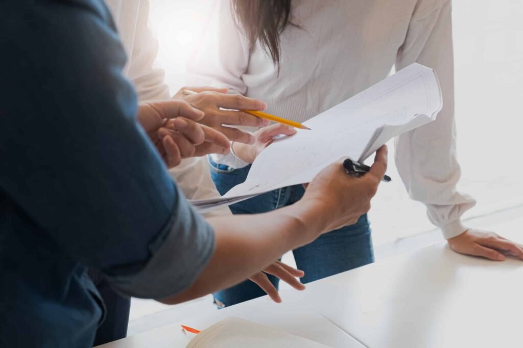 Deux personnes examinent et discutent des documents sur un bureau, l'une tenant des papiers et un stylo, l'autre faisant des gestes avec un crayon.
