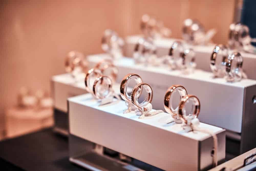 Plusieurs bagues en or et en argent sont exposées sur des présentoirs blancs dans une bijouterie.