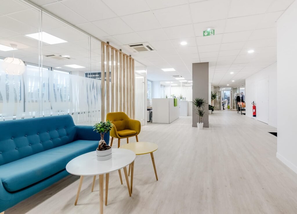 Une salle d'attente de bureau moderne avec un canapé bleu, un fauteuil jaune et de petites tables.
