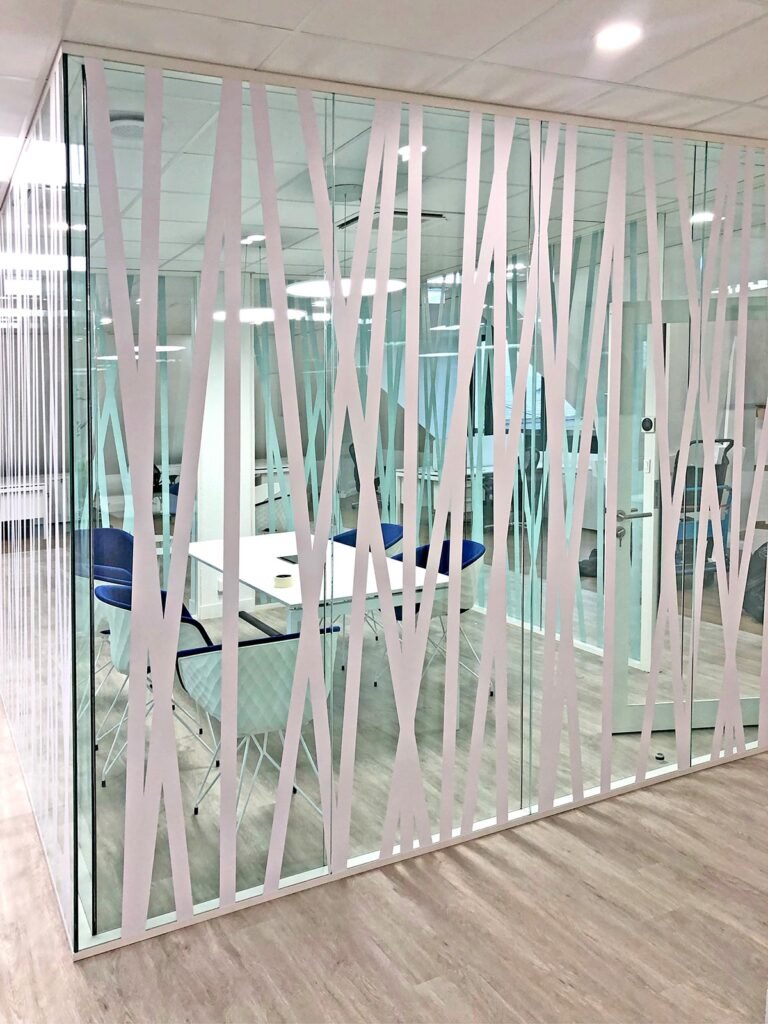 Salle de réunion de bureau vitrée avec des motifs croisés blancs, une table blanche, des chaises bleues et un sol d'aspect bois, vue de l'extérieur de la salle.