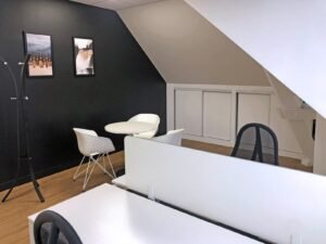 Bureau moderne avec des bureaux blancs, des chaises noires, une petite table ronde avec deux chaises blanches, de l'art mural et un porte-manteau contre un mur d'accent noir.
