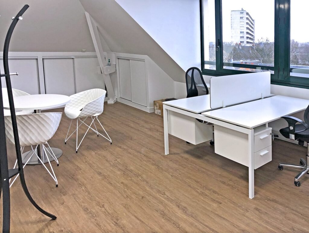 Bureau moderne avec deux bureaux blancs, deux chaises de bureau, une petite table ronde avec trois chaises blanches, un porte-manteau, un sol en bois et une grande fenêtre donnant sur les bâtiments.