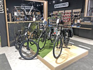 Quatre bicyclettes sont exposées sur une plate-forme surélevée dans un magasin, avec divers accessoires de cyclisme accrochés au mur derrière elles.