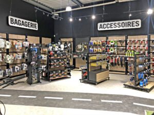 L'intérieur d'un magasin de détail présente des étagères remplies de sacs, de casques et de divers accessoires sous des enseignes indiquant "Bagagerie" et "Accessoires".