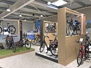 Une salle d'exposition de bicyclettes avec différents vélos exposés sur des supports et des plates-formes, un éclairage moderne et des affiches sur le cyclisme sur les murs.