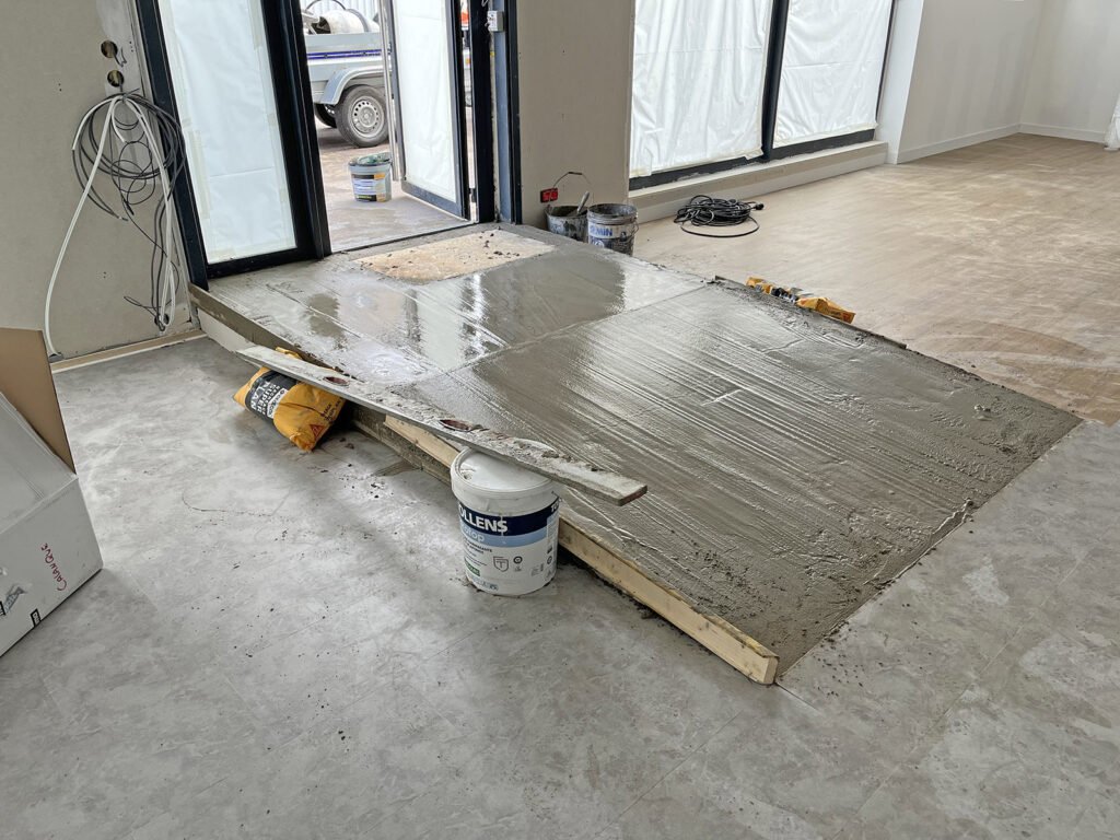 Une rampe en béton récemment coulée à l'intérieur d'un bâtiment, avec des matériaux de construction et des outils visibles à proximité.