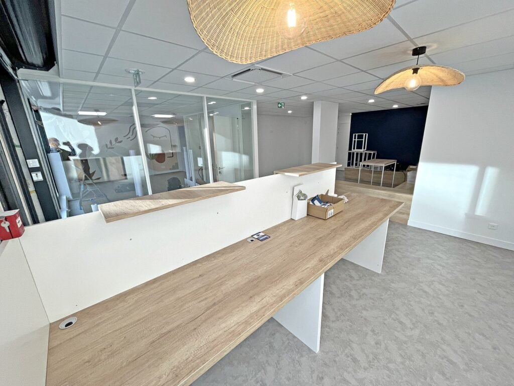 Réception dans un bureau moderne avec des accents en bois, des lampes suspendues, des pièces vitrées et quelques articles non emballés sur le comptoir.