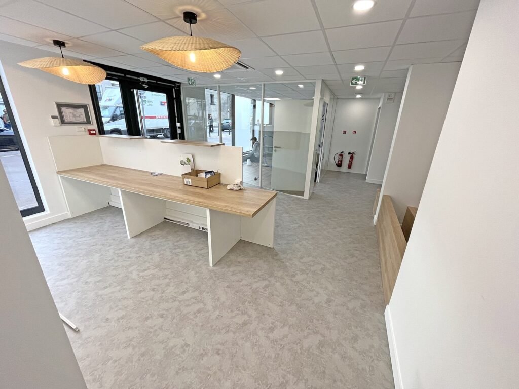 Réception de bureau moderne avec un bureau en bois, des cloisons en verre et des lampes suspendues.
