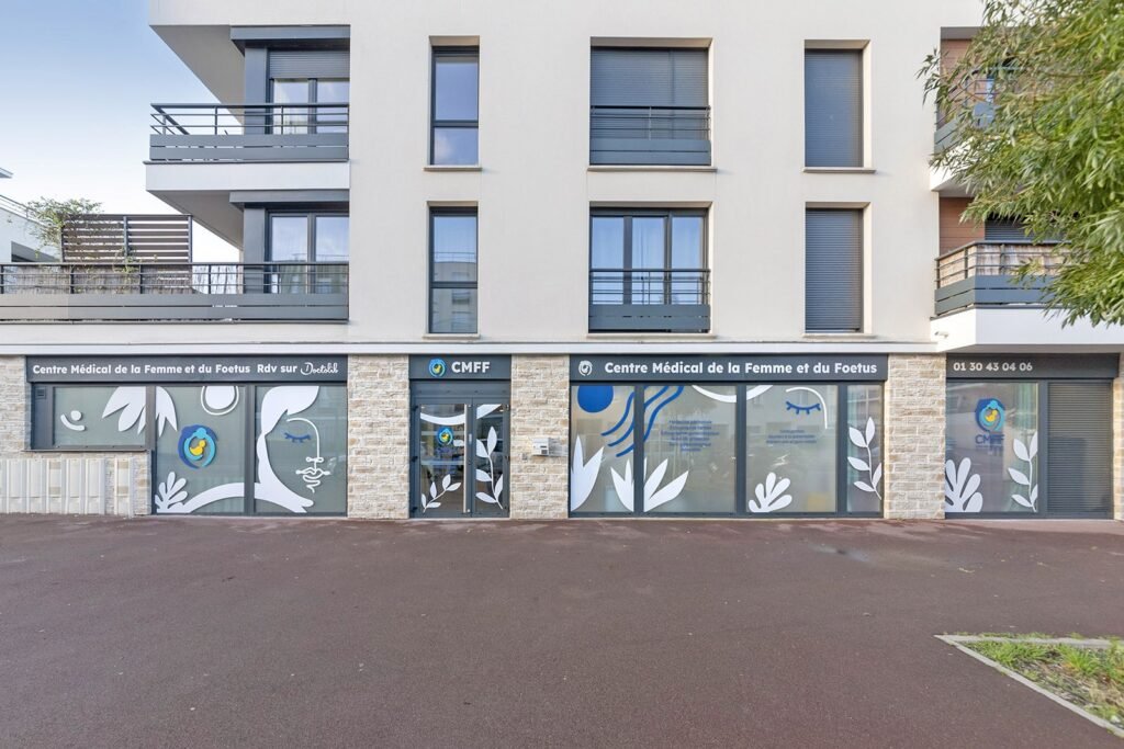 Vue de la rue du Centre Médical de la Femme et du Foetus, avec de grandes fenêtres aux motifs inspirés de la nature et une signalétique en français.