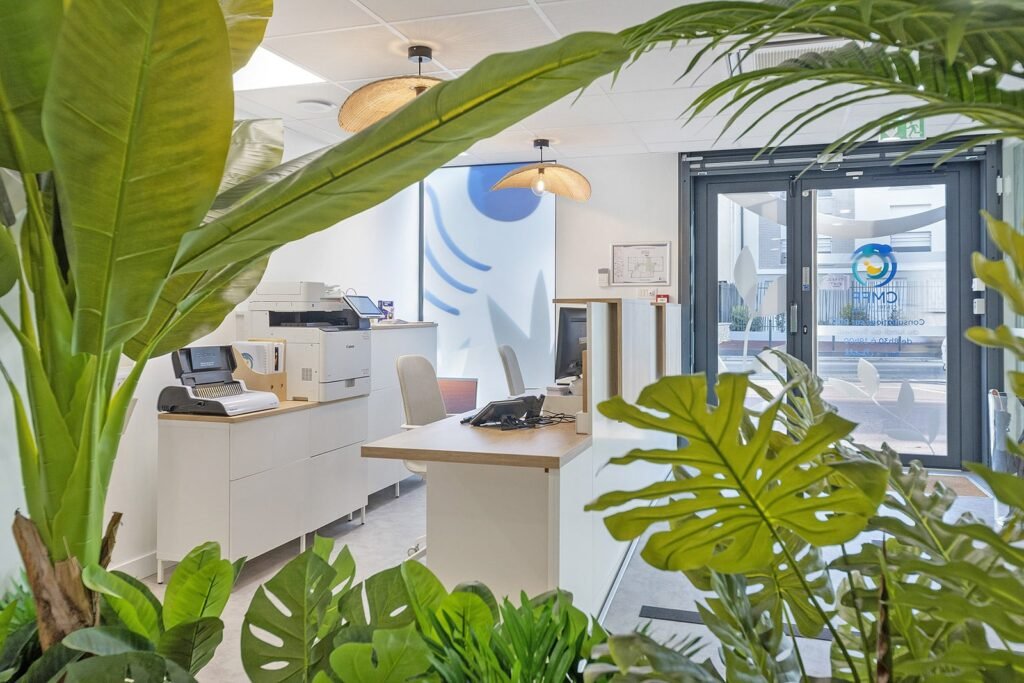 Espace de réception d'un bureau avec des plantes, une imprimante et des bureaux.