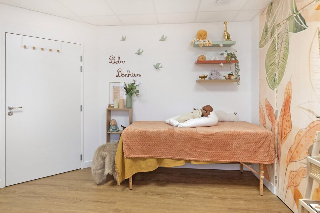 Une chambre d'enfant minimaliste avec une table à langer, une poupée, de l'art mural décoratif, des étagères avec des jouets et des plantes, et un papier peint avec de grands motifs botaniques.
