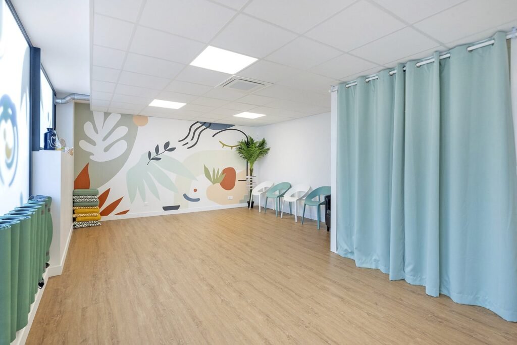 Une pièce moderne et lumineuse avec un sol en bois, une peinture murale abstraite sur le mur, des chaises bleues, une plante en pot et des rideaux bleus du sol au plafond.