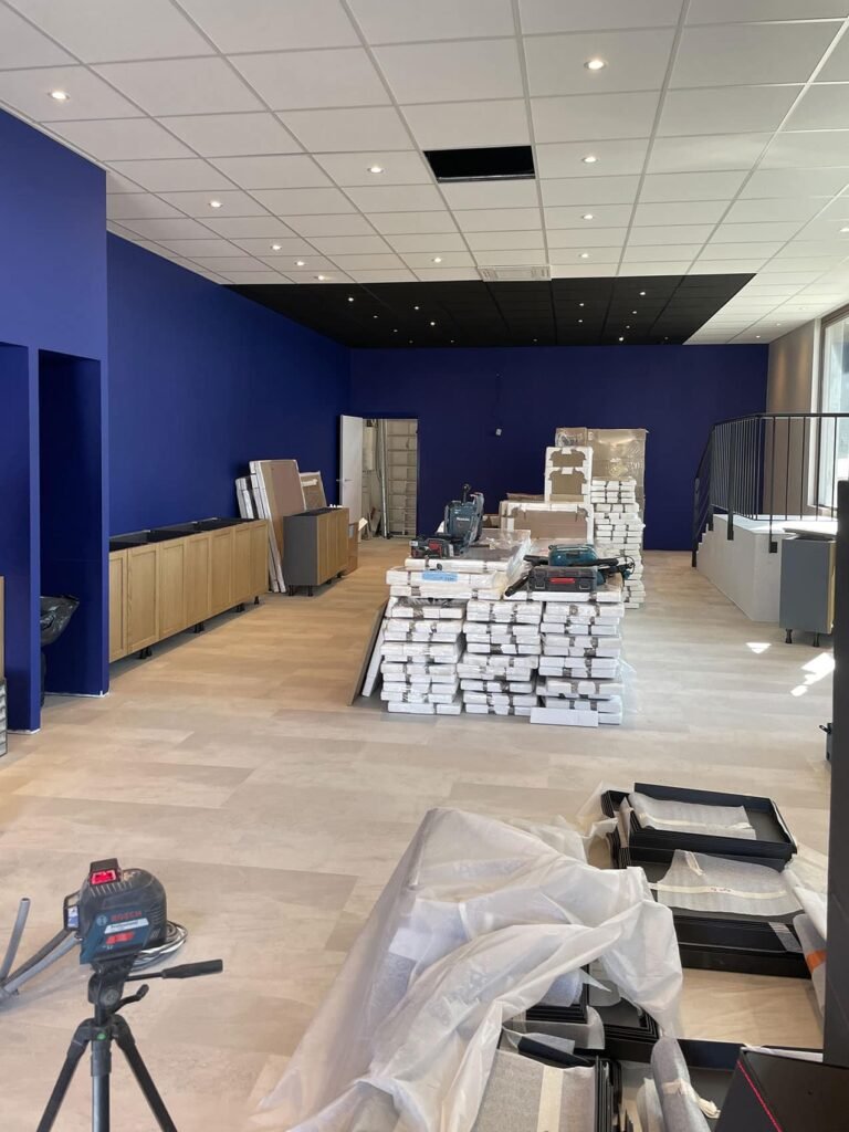 Chantier de construction intérieur avec des murs bleus, un sol inachevé et des matériaux empilés.