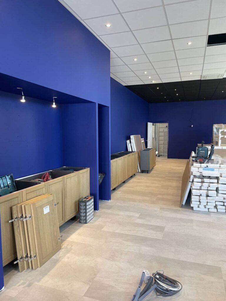 Une pièce en cours de rénovation avec des murs bleus, un sol en bois clair, des meubles en cours d'installation et des matériaux de construction éparpillés.