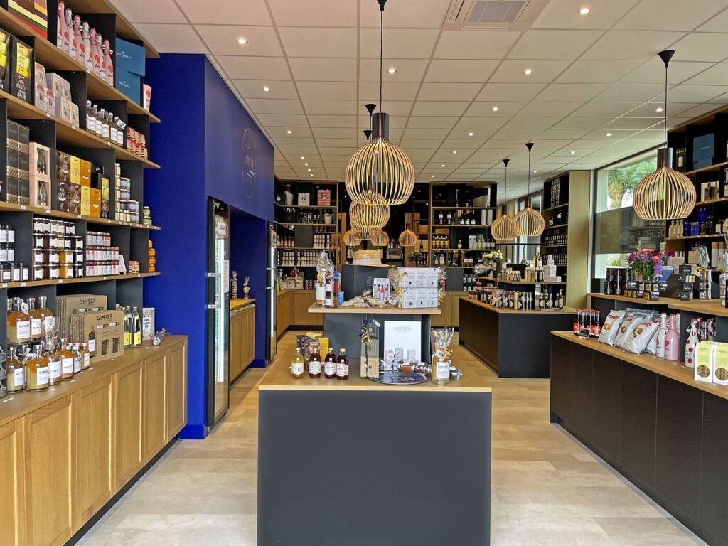 Magasin moderne de produits alimentaires et de boissons avec des étagères en bois, des lampes suspendues et divers produits présentés proprement sur les comptoirs et les murs.