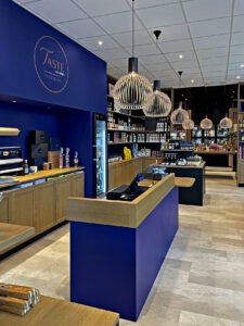 Intérieur d'une épicerie fine moderne avec des étagères en bois, des comptoirs bleus, des lampes suspendues et des présentoirs de divers produits alimentaires emballés.