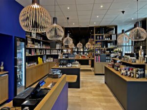 Intérieur d'une épicerie fine moderne avec des étagères en bois, des lampes suspendues et divers produits emballés présentés dans l'espace.