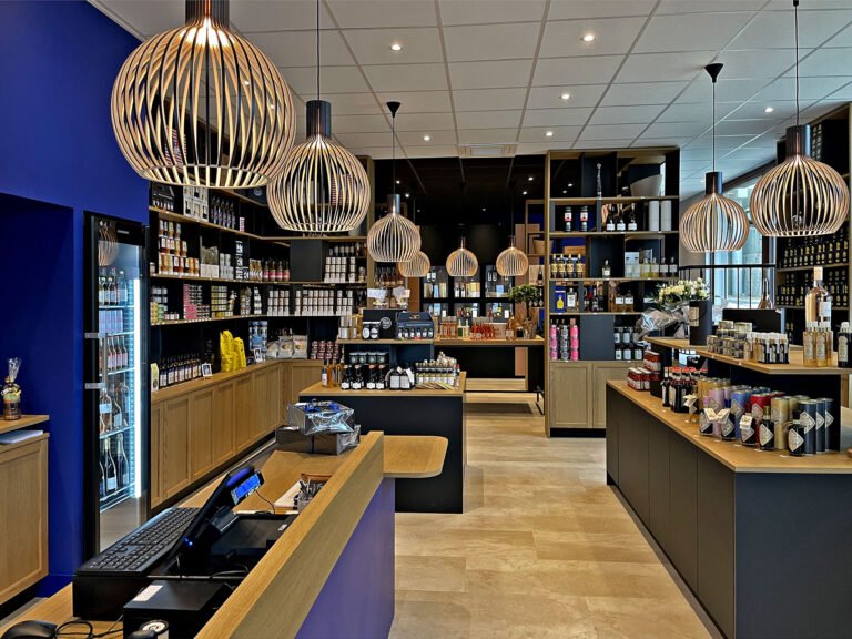 Intérieur d'une épicerie fine moderne avec des étagères en bois, des lampes suspendues et divers produits emballés présentés dans l'espace.