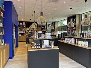 Intérieur d'un magasin spécialisé moderne avec des étagères et des présentoirs de produits gastronomiques, de boissons et d'articles de cadeaux sous des lumières suspendues, avec des produits bien organisés dans tout l'espace.