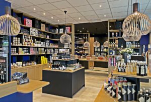 Intérieur moderne d'un magasin de vins et de produits alimentaires spécialisés, avec des étagères remplies de bouteilles, de bocaux et de produits gastronomiques, sous des lampes suspendues et un étalage bien organisé.