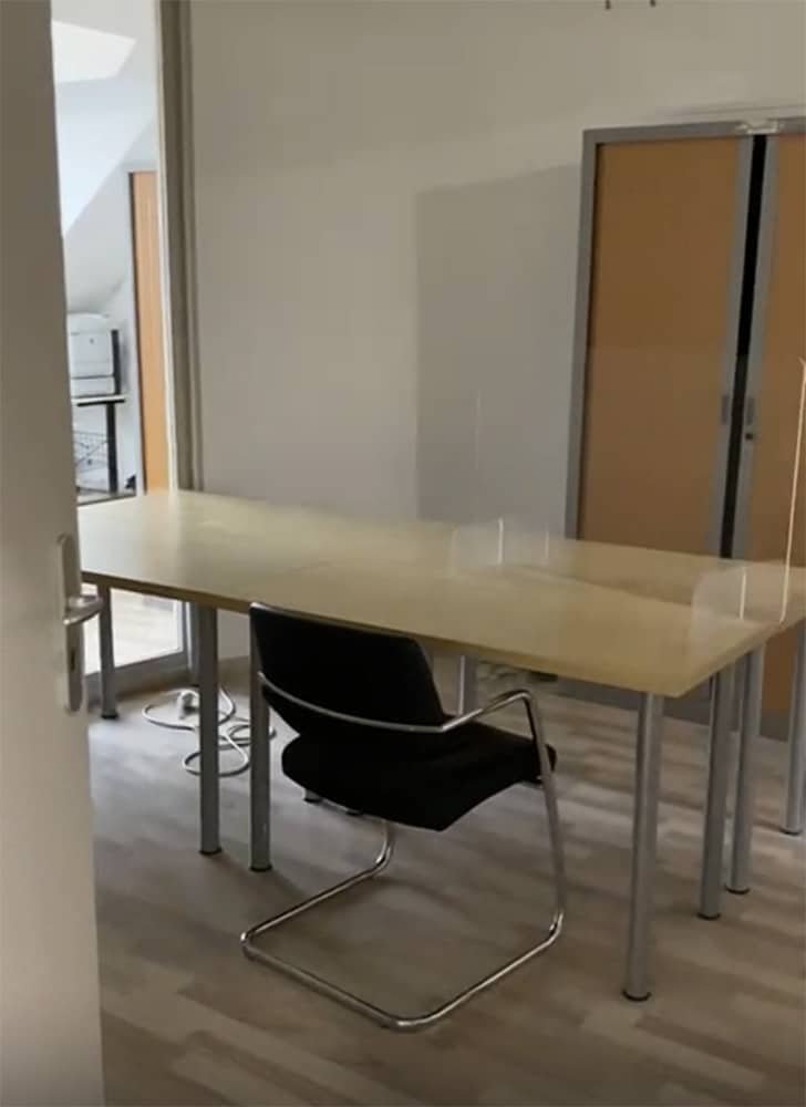Une longue table avec une chaise et des séparateurs transparents est présentée dans un bureau.