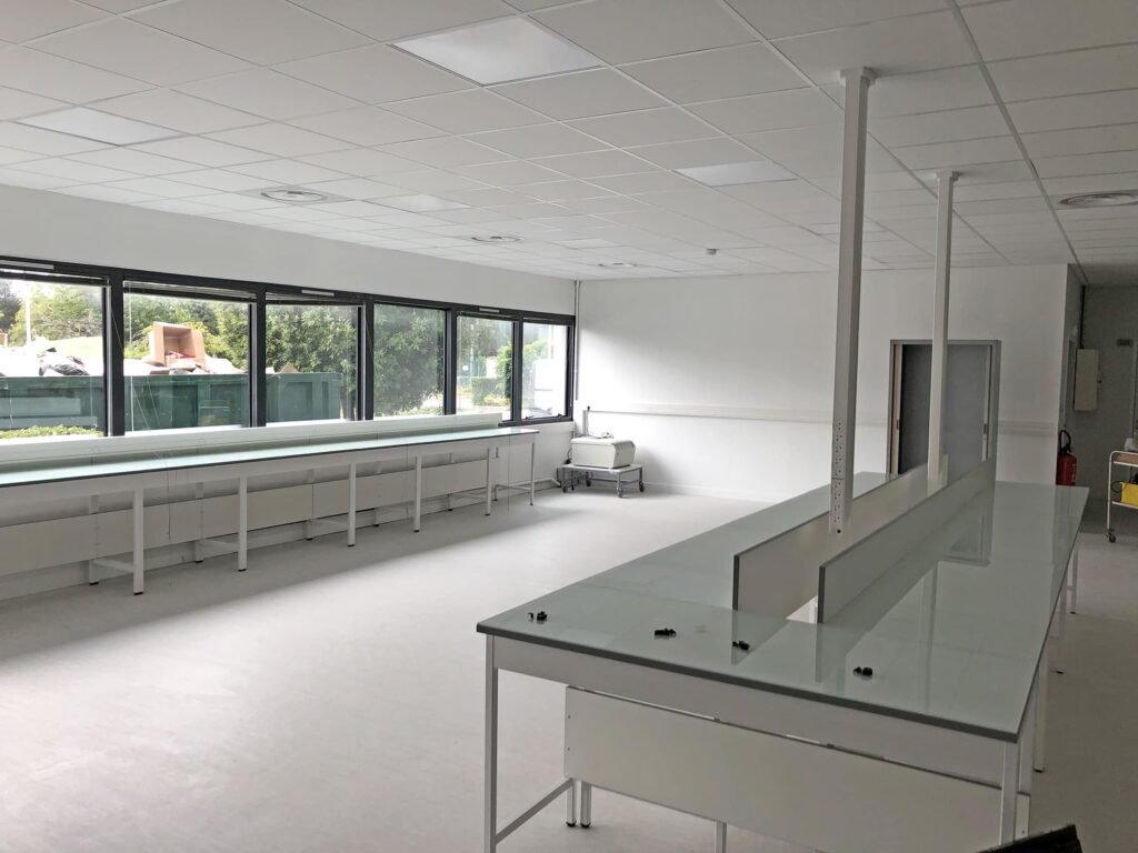 Un laboratoire spacieux et vide avec des murs blancs, de grandes fenêtres, de longues tables de travail et des plafonniers.