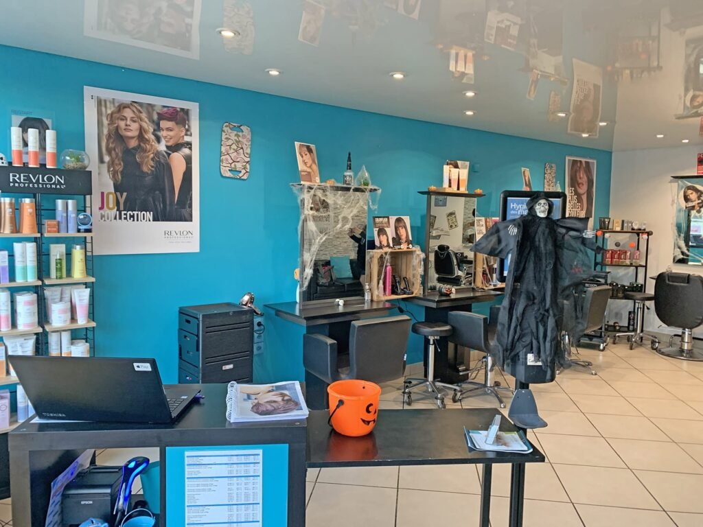 Un salon de coiffure aux murs bleus, avec des étagères de produits capillaires, des postes de coiffure et des décorations d'Halloween, dont un fantôme suspendu et un seau à citrouille orange.