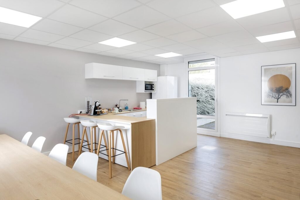 Cuisine et salle à manger modernes avec placards blancs, sol en bois, tabourets de bar, table de salle à manger, œuvres d'art murales et grande fenêtre laissant entrer la lumière naturelle.