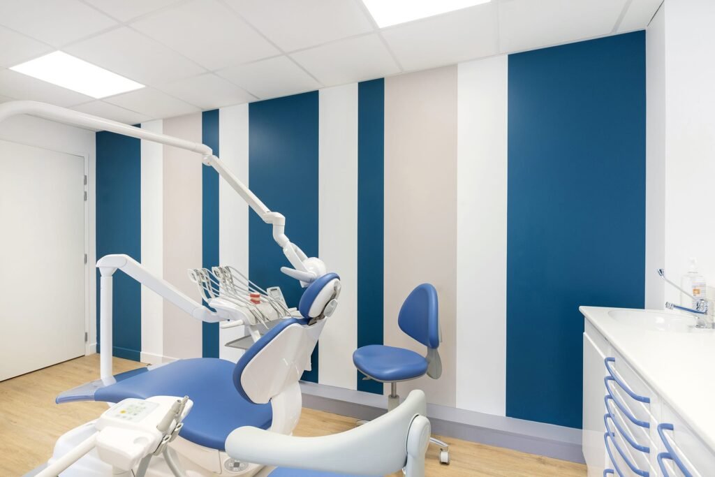 Une salle d'examen dentaire moderne avec un mur rayé bleu et blanc, un fauteuil dentaire et un lavabo.