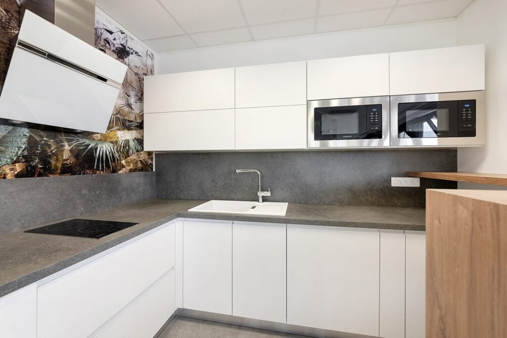 Cuisine moderne avec des armoires blanches, un comptoir gris, un évier encastré, une cuisinière, deux micro-ondes muraux et un dosseret décoratif sur le thème de la nature.