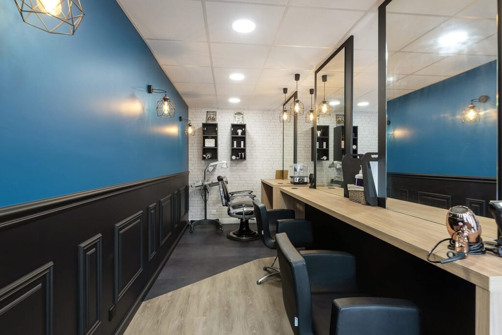 Intérieur d'un salon de coiffure avec des murs bleus et noirs, des miroirs, des fauteuils de coiffeur et un comptoir en bois.