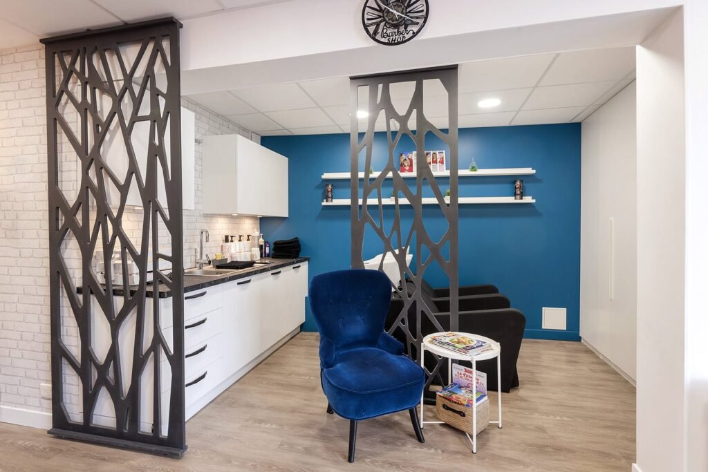 Intérieur de salon moderne avec un mur d'accent bleu, deux chaises noires, un fauteuil bleu, une petite table ronde avec des magazines et des cloisons décoratives noires.