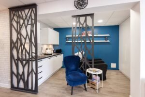 Intérieur de salon moderne avec un mur d'accent bleu, deux chaises noires, un fauteuil bleu, une petite table ronde avec des magazines et des cloisons décoratives noires.