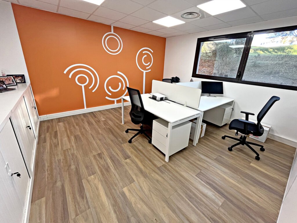 Bureau moderne avec deux bureaux, des chaises de bureau, des ordinateurs, une grande fenêtre, du parquet et un mur d'accent orange avec des motifs blancs minimalistes.