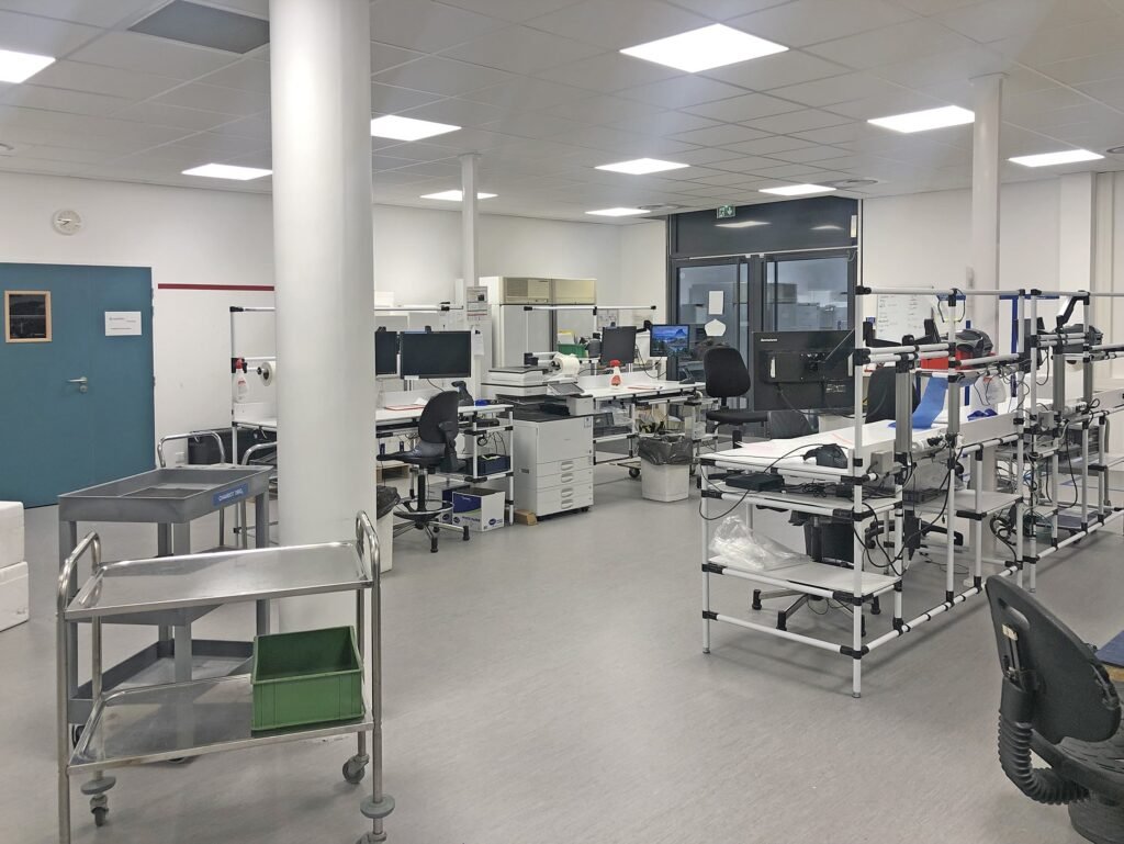 Un laboratoire propre et moderne avec des postes de travail, du matériel de laboratoire, des ordinateurs, des chariots roulants et diverses fournitures organisées dans la pièce.