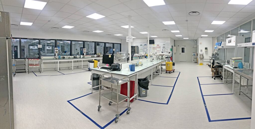 Laboratoire spacieux équipé de postes de travail, de matériel, de chariots et de poubelles, doté d'un éclairage zénithal lumineux et de zones marquées au sol.