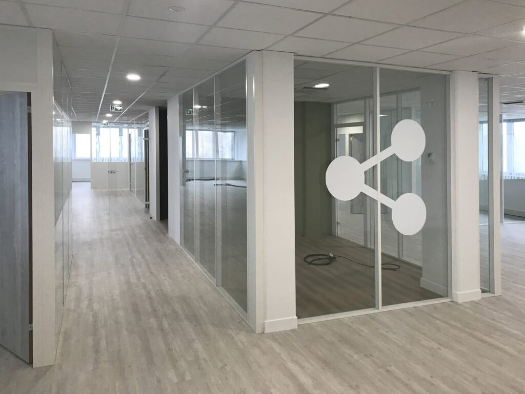 Couloir de bureau moderne avec des murs en verre, un sol en bois clair et une grande icône de réseau blanche sur la fenêtre d'une salle de réunion.