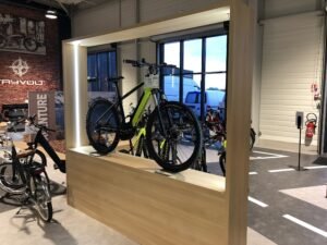 Un vélo tout-terrain vert présenté sur une plate-forme en bois dans une salle d'exposition, avec d'autres vélos visibles à l'arrière-plan.