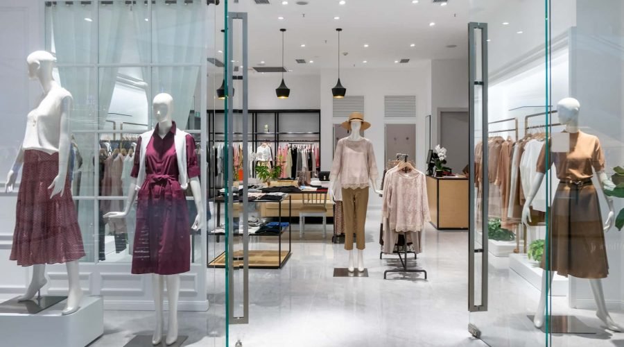 Intérieur d'un magasin de vêtements avec des mannequins présentant des tenues féminines près de l'entrée vitrée ; des étagères de vêtements et d'accessoires sont disposées dans l'espace bien éclairé.