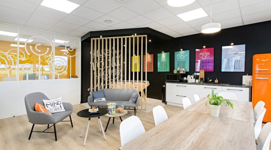 Salle de pause d'un bureau moderne avec un canapé gris, des chaises, un comptoir de cuisine et un réfrigérateur rétro orange.