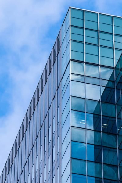 Immeuble de bureaux moderne en verre avec des fenêtres réfléchissantes sur fond de ciel bleu avec des nuages.