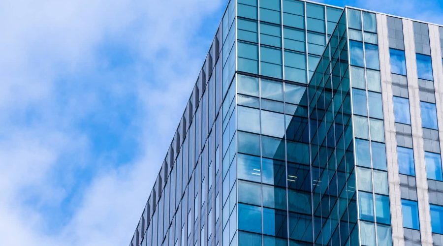 Immeuble de bureaux moderne en verre avec des fenêtres réfléchissantes sur fond de ciel bleu avec des nuages.
