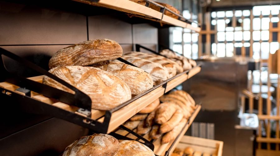 Des miches de pain rustique sont présentées sur des étagères en bois dans une boulangerie à l'intérieur moderne et à la lumière naturelle, mettant en valeur l'agencement expert de la boulangerie pour une atmosphère accueillante.