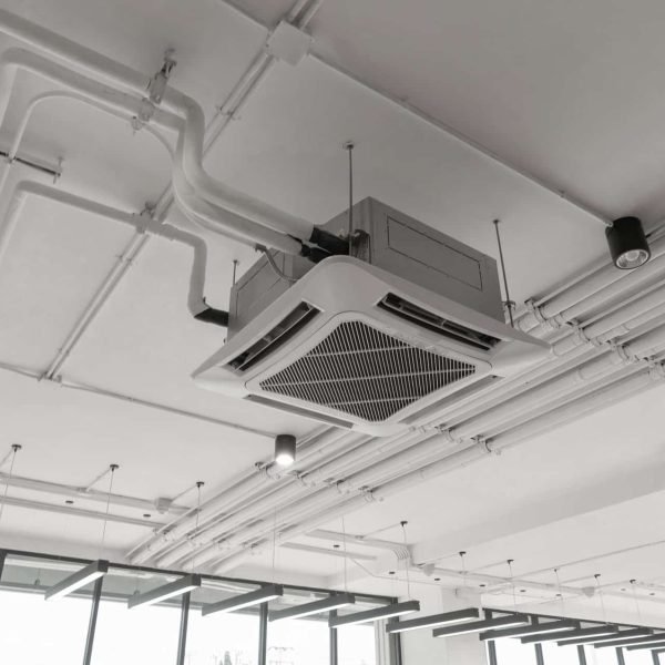 Unité de climatisation à cassette montée au plafond avec des tuyaux apparents et plusieurs plafonniers dans un espace commercial moderne.