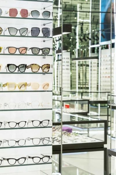 Étagères remplies de montures de lunettes de différents styles et couleurs dans un magasin d'optique bien éclairé.