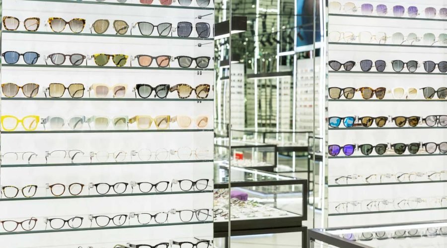 Étagères remplies de montures de lunettes de différents styles et couleurs dans un magasin d'optique bien éclairé.