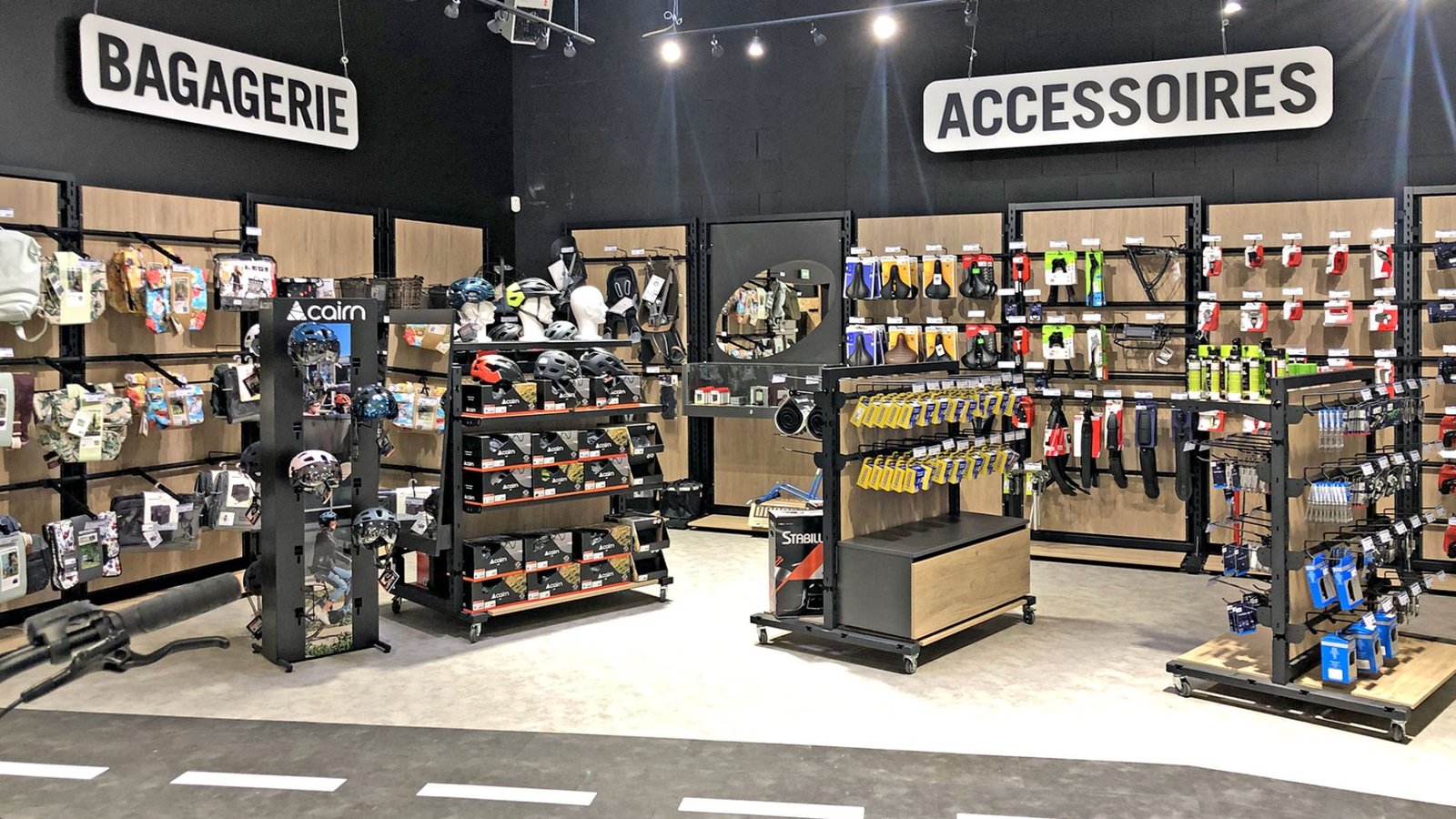 L'intérieur d'un magasin de détail présente des étagères remplies de sacs, de casques et de divers accessoires sous des enseignes indiquant "Bagagerie" et "Accessoires".